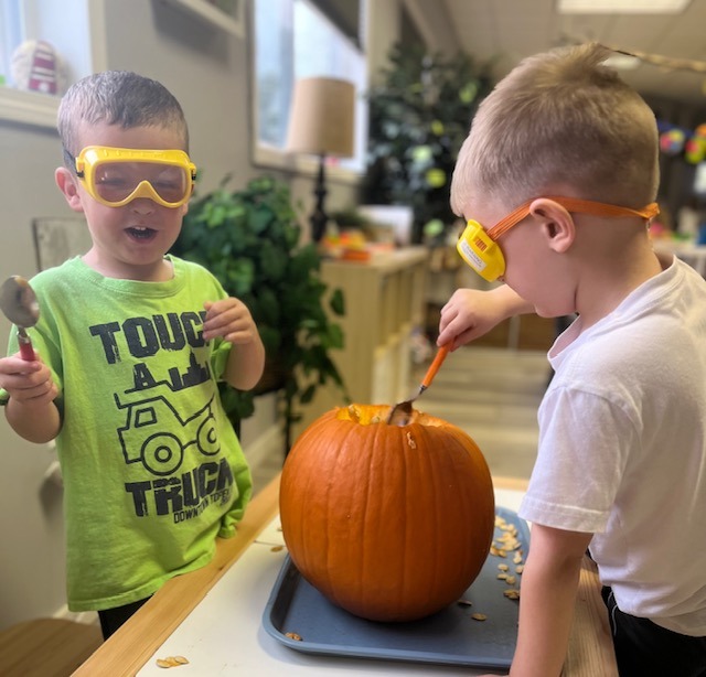 Two boys carving a pumpkin with safety goggles